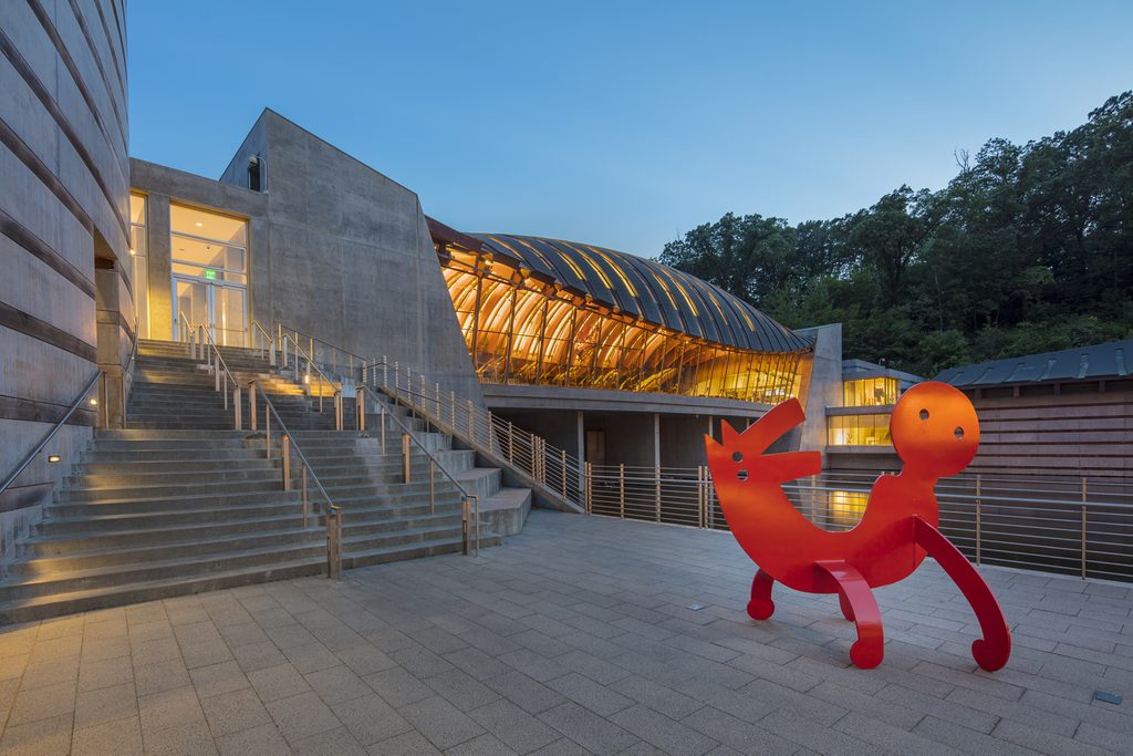Modern building with concrete walls and a curved glass facade, featuring a red abstract sculpture.