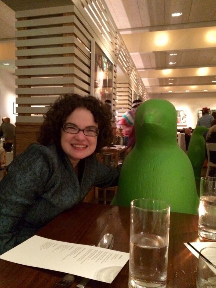 Amy Torbert, Tyson Scholar Person with large green penguin statue at a restaurant table with menu and water glasses.