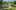 Circular stone structure with steps, grassy area, trees, and curved path with stone wall.