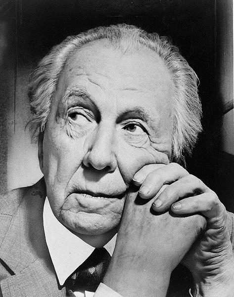 Elderly person with suit and tie, light hair, resting chin on hands, contemplative expression.