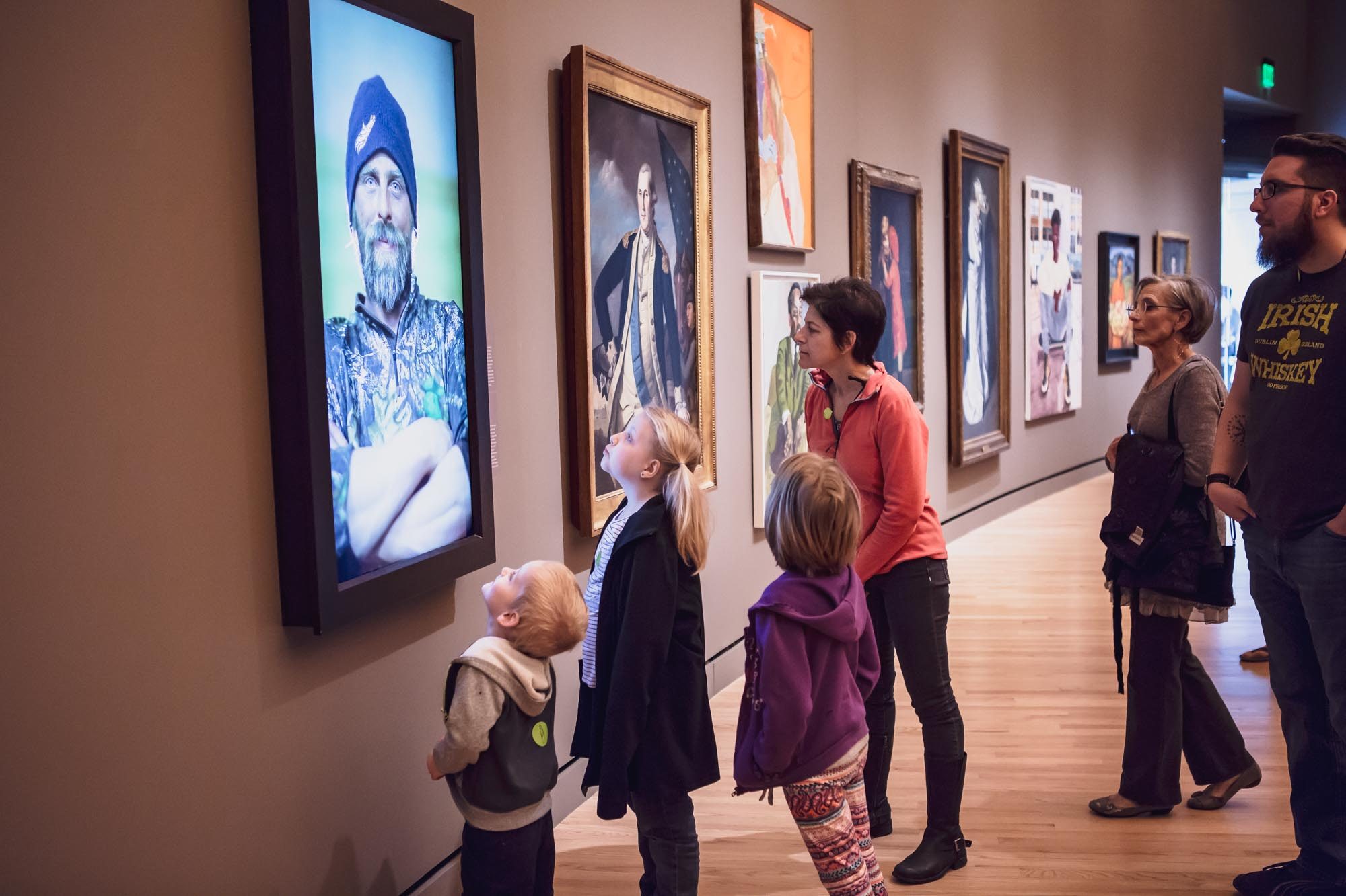 Guest look at art in the Early American Gallery Group in gallery viewing digital and traditional art displays on modern wooden flooring.