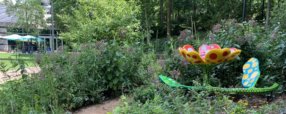 A large, colorful flower sculpture with polka dots made of painted steel sits low to the ground