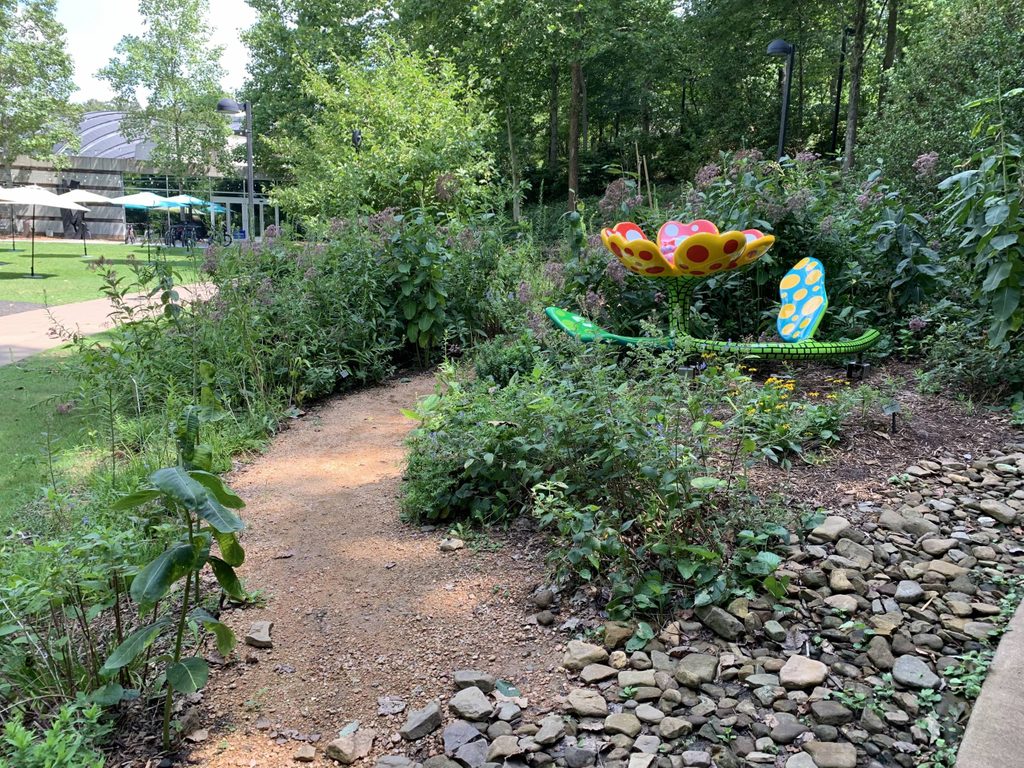 A large, colorful flower sculpture with polka dots made of painted steel sits low to the ground