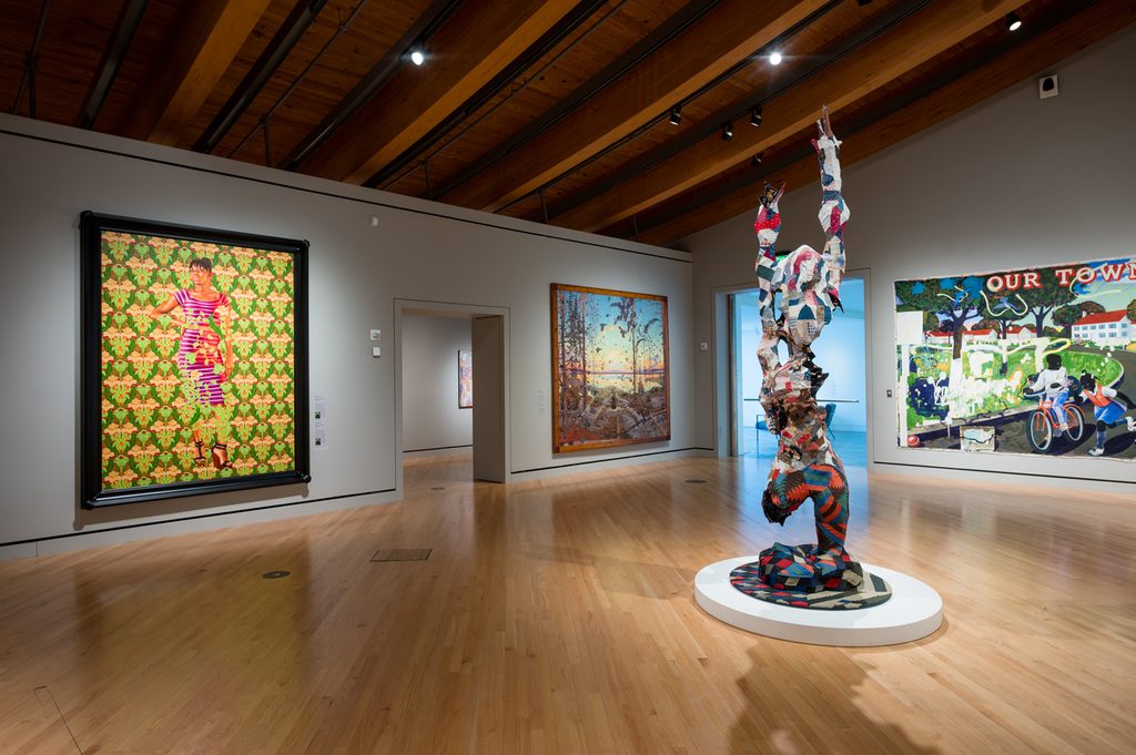 Art gallery with wooden ceilings, diverse artworks, colorful paintings, and abstract sculpture.
