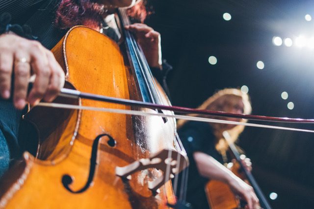 Musicians playing cellos on stage with a backdrop of stars or stage lights.
