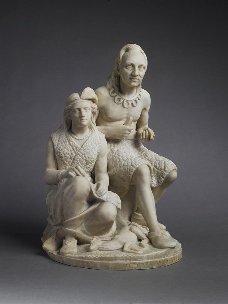Marble sculpture of two seated figures in textured clothing with necklaces, and a small animal.